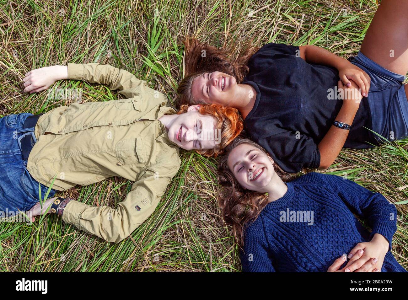 Vacanze estive vacanza felice persone concetto. Vista dall'alto gruppo di tre amici che si trovano sull'erba in cerchio sorridendo e divertirsi insieme all'aperto. Picnic con gli amici in viaggio in natura Foto Stock