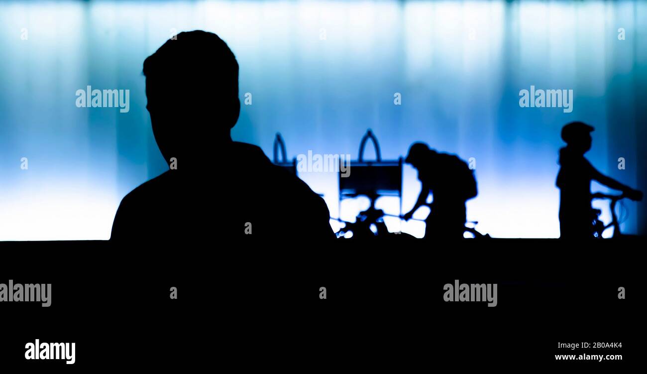 Silhouette di giovane uomo in primo piano nella notte e persone con moto dietro di lui , di fronte al moderno edificio in contrasto nero e blu bianco Foto Stock