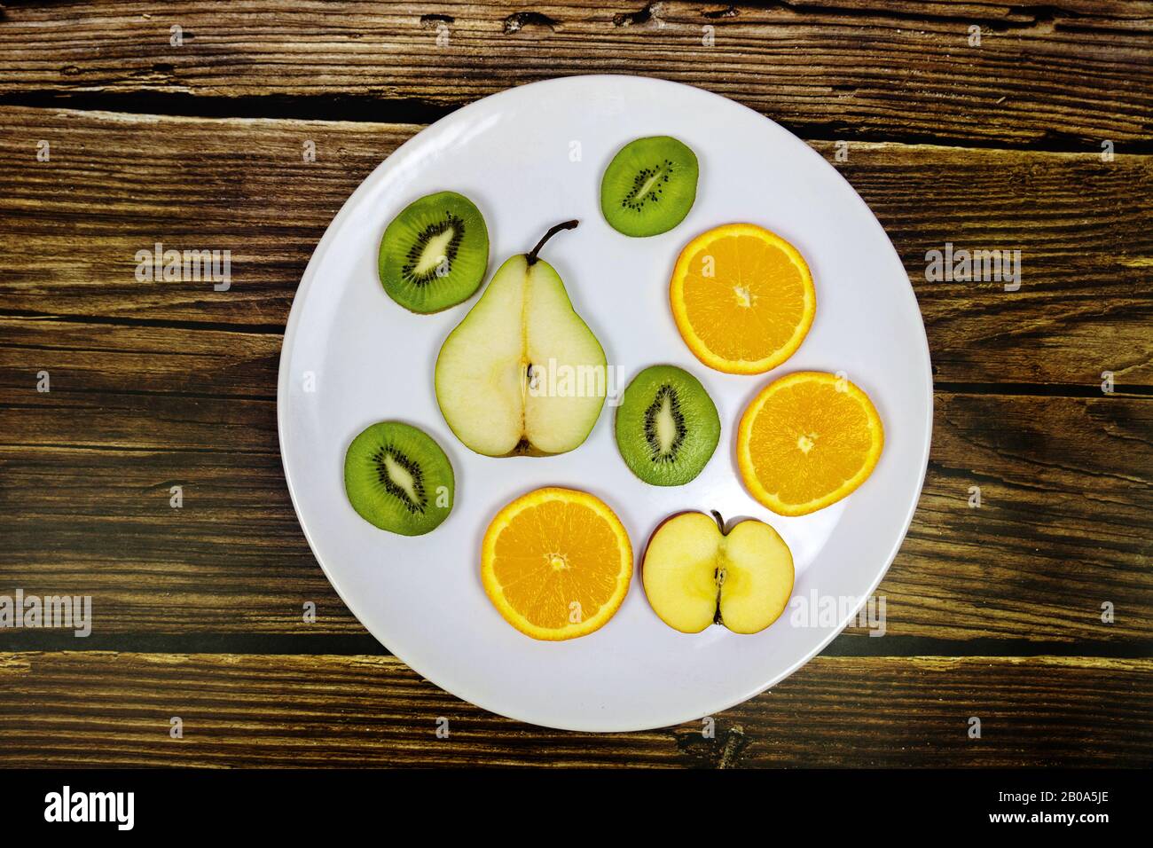 frutta a fette pera kiwi mela arancione su un piatto bianco witg rustico sfondo di legno Foto Stock