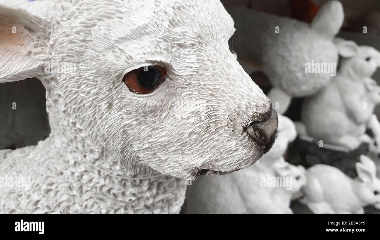 Primo piano di pietra di agnello figurina, tradizionale decorazione casa di Pasqua, in background un gruppo di conigli di pietra fuori fuoco. Foto Stock