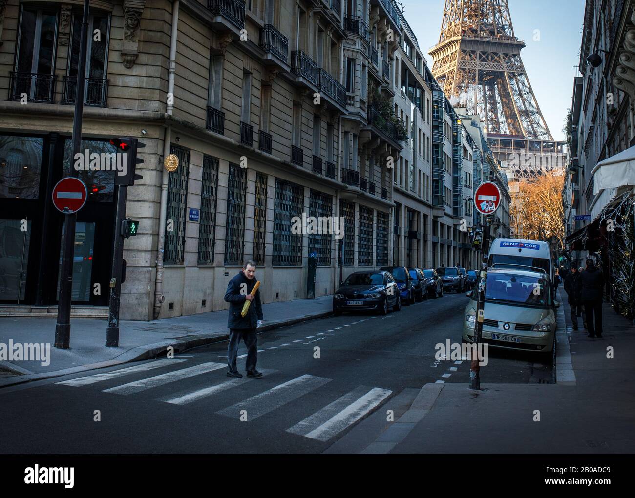 Un uomo cammina con la sua baguette passando davanti alla Torre Eiffel a Parigi, Francia. Foto Stock