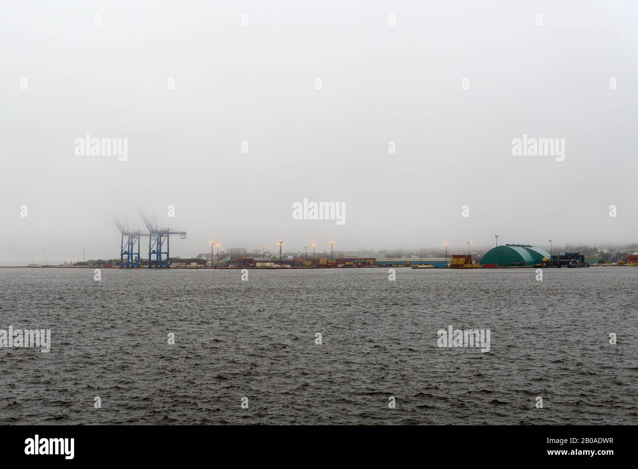 Vista ad ampio angolo del porto di San Giovanni in alta marea. L'acqua è così alta che è quasi sopra le banchine. La parte superiore delle gru è nascosta dalla nebbia. Foto Stock