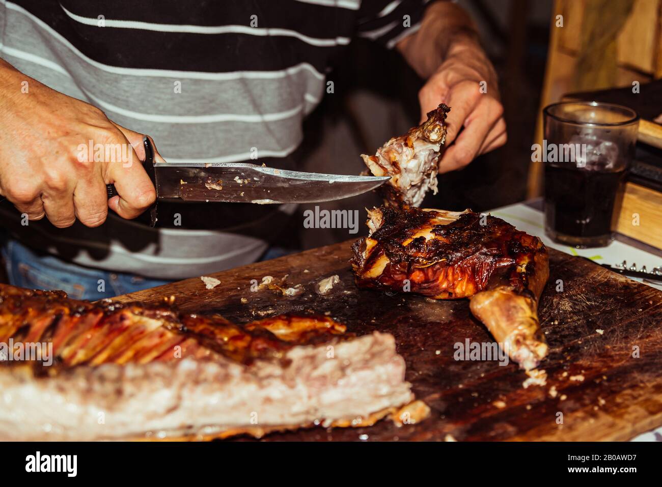 Lo chef taglia il maiale alla griglia in bistecche con coltello. Tradizionale maialino da latte cotto sulla griglia a carbone. Il piccolo maiale è arrostito intero su uno o Foto Stock