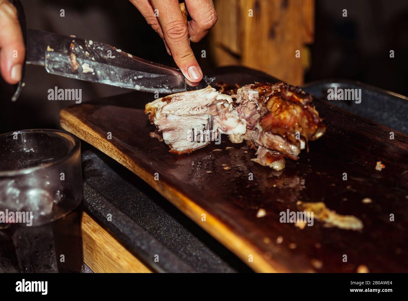 Lo chef taglia il maiale alla griglia in bistecche con coltello. Tradizionale maialino da latte cotto sulla griglia a carbone. Il piccolo maiale è arrostito intero su uno o Foto Stock