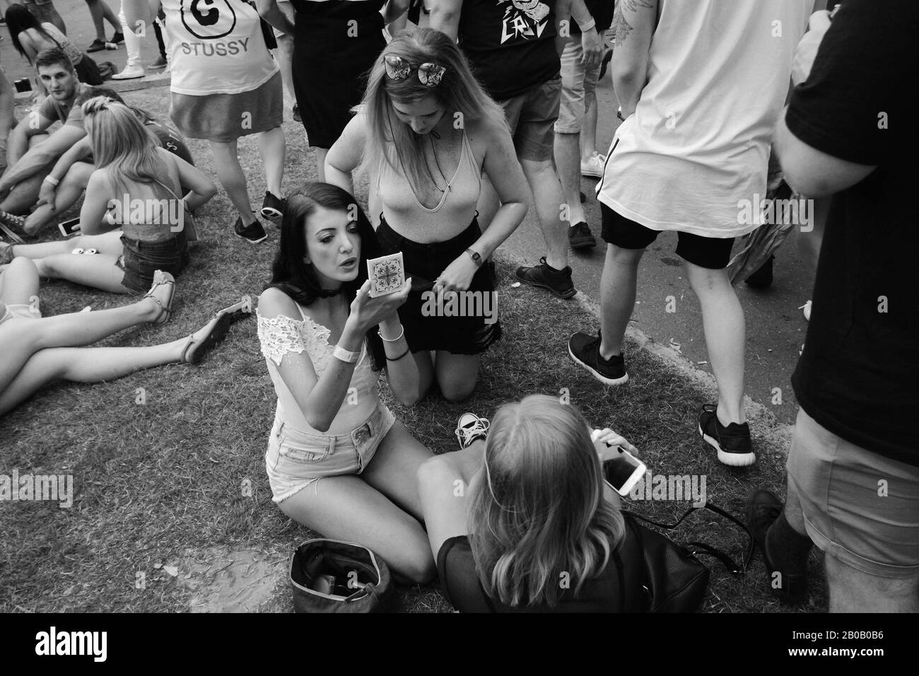 Donne in abbigliamento estivo fare make-up seduto sul prato, altri gruppi nelle vicinanze - Documentando un festival musicale Sydney, Australia Foto Stock