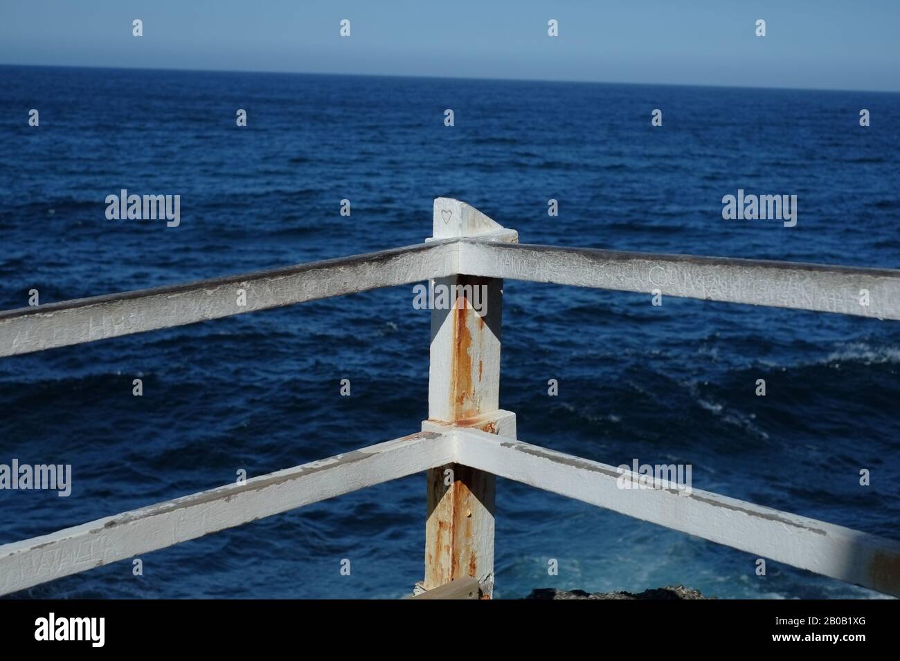Un cuore d'amore scolpito nel palo di legno e la ferrovia graffiata della recinzione di sicurezza della cima della scogliera con una vista dell'oceano, Bronte Beach, Sydney Foto Stock