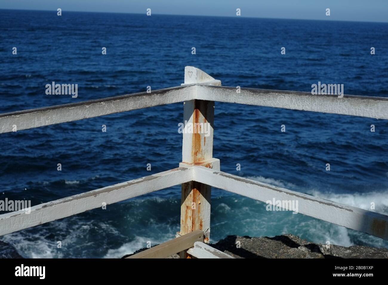 Un cuore d'amore scolpito nel palo di legno e la ferrovia graffiata della recinzione di sicurezza della cima della scogliera con una vista dell'oceano, Bronte Beach, Sydney Foto Stock