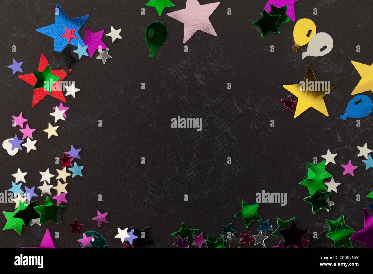 Festa confetti stelle e forma di tutti i colori sparsi su un tavolo nero con spazio copia Foto Stock