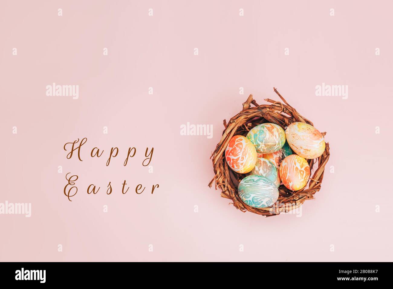 Le uova di pasqua Coloseful nel nido su sfondo di colore rosa pastello. Foto Stock