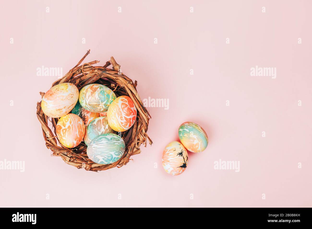 Le uova di pasqua Coloseful nel nido su sfondo di colore rosa pastello. Foto Stock