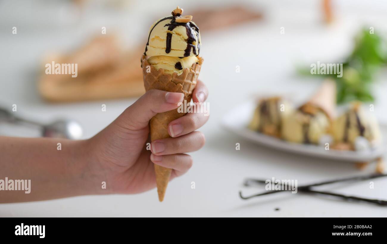 Vista ravvicinata di una ragazza che tiene il cono gelato alla vaniglia con sciroppo di cioccolato gocciolato in cima Foto Stock