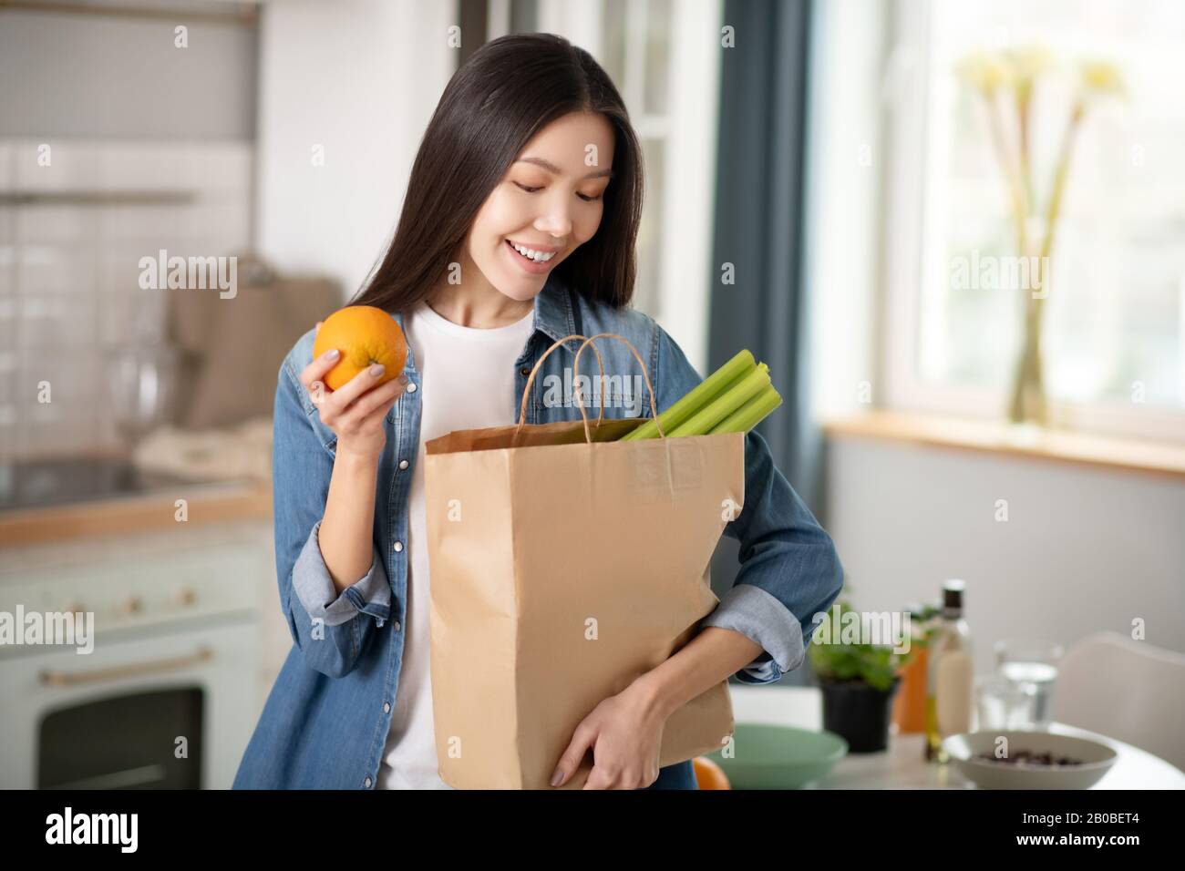 Bella donna con arancia in mano guardando in borsa con verdure. Foto Stock