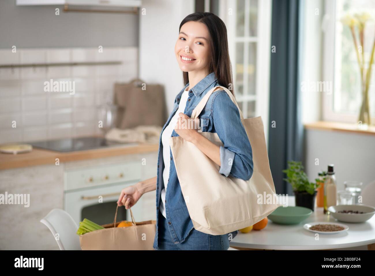 Giovane donna sorridente con borse ecologiche a casa. Foto Stock