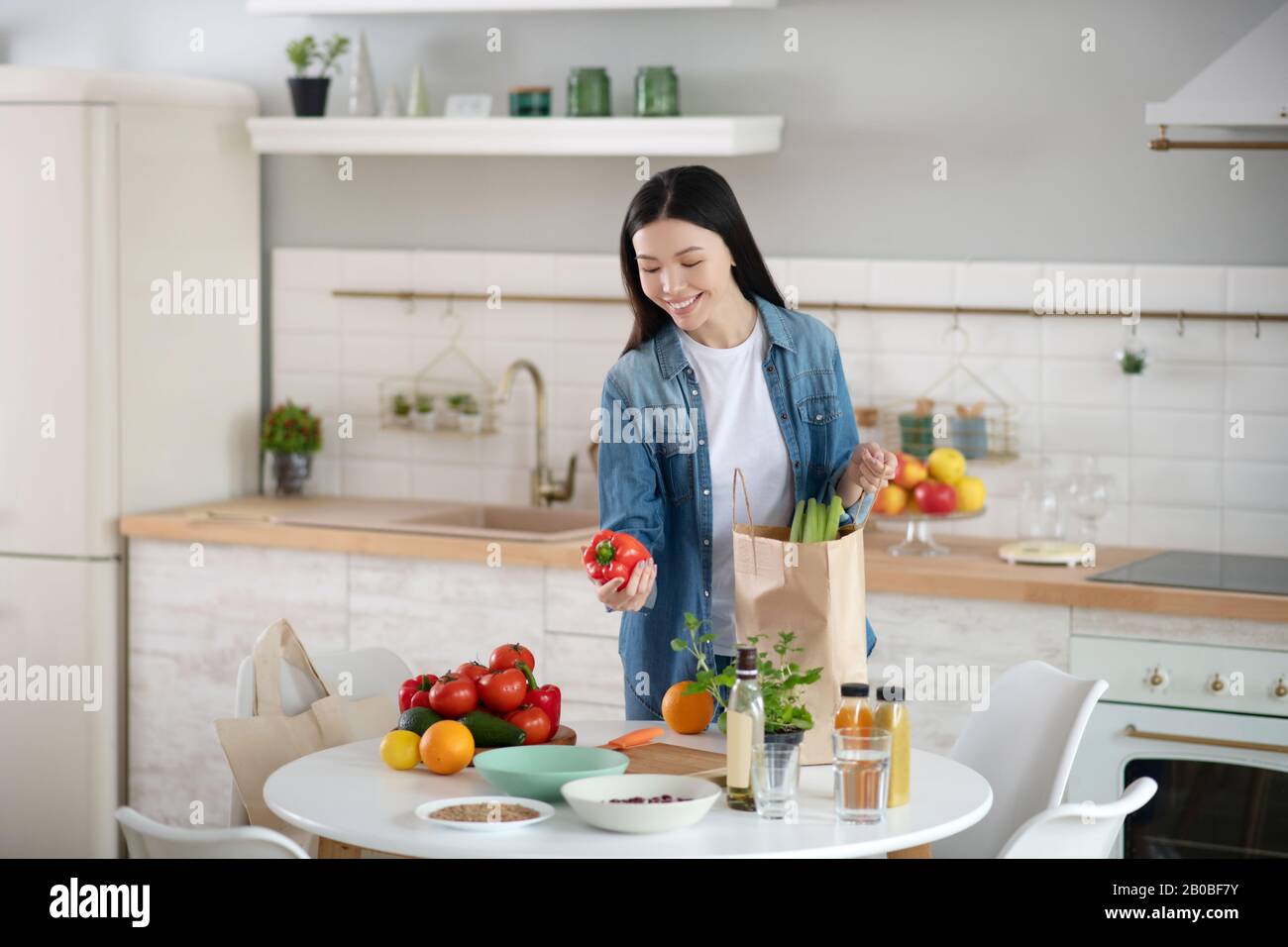 Giovane donna di fronte al tavolo da cucina con verdure e frutta. Foto Stock