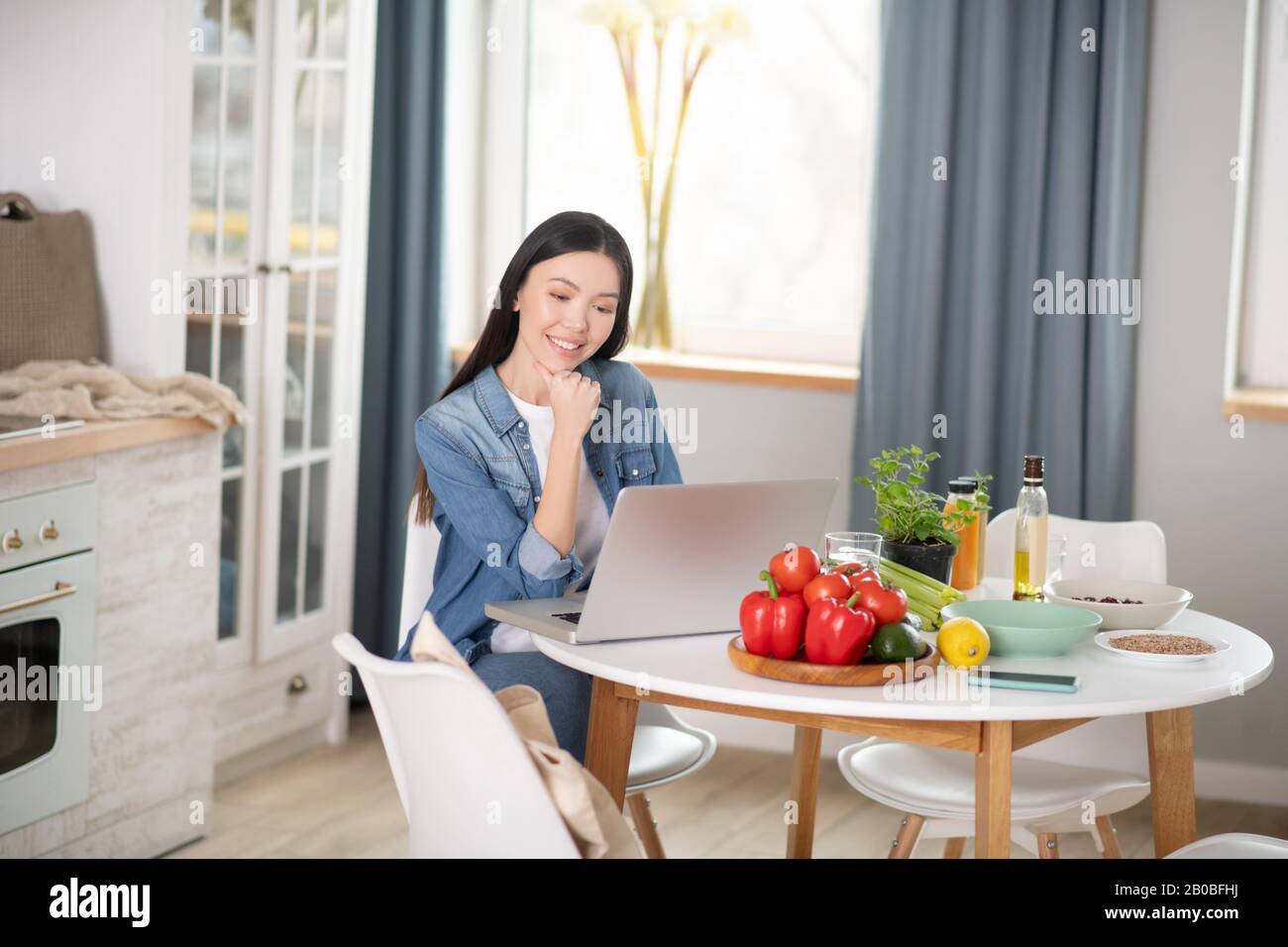 Ragazza giovane seduto al tavolo da cucina con un computer portatile. Foto Stock