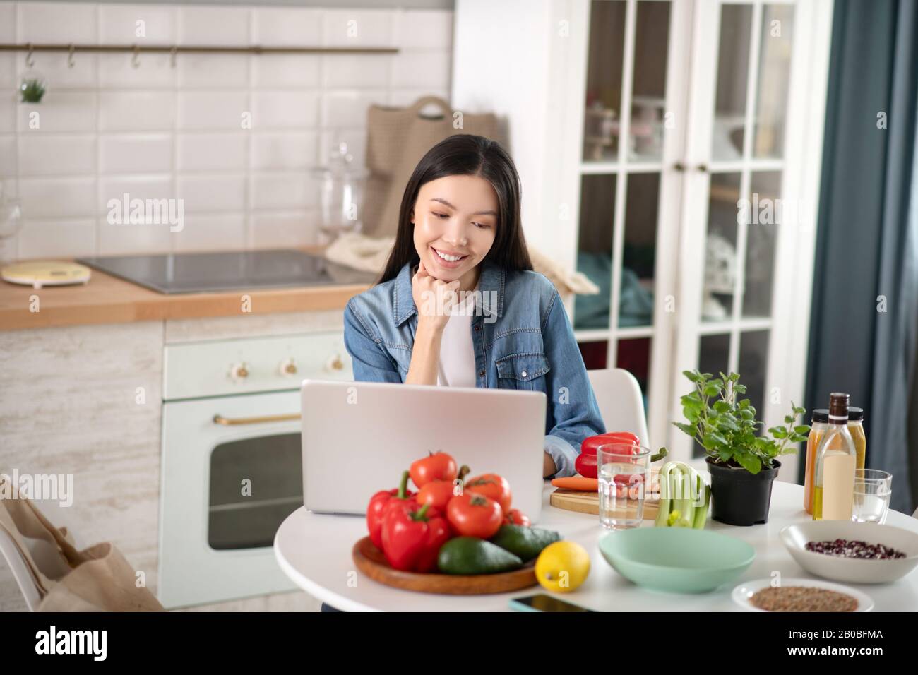 Giovane donna seduto su un computer portatile in cucina. Foto Stock