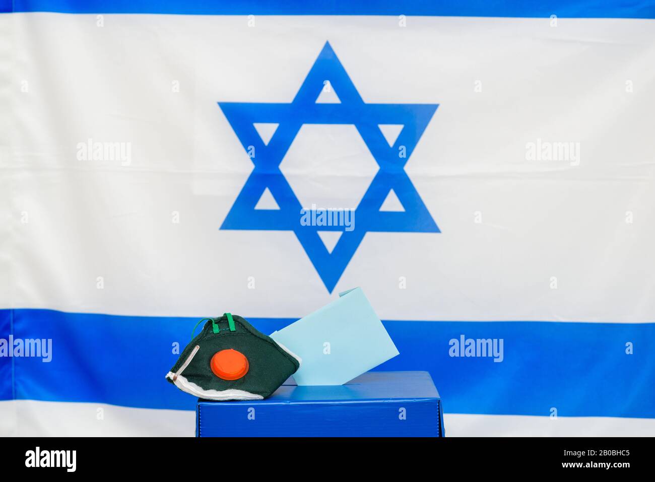 Elezioni Israele. Maschera facciale respiratoria batterica in una scatola per le elezioni in Israele sfondo bandiera. Gli israeliani messi in quarantena per il coronavirus avranno le cabine di voto per le elezioni di marzo. Foto Stock