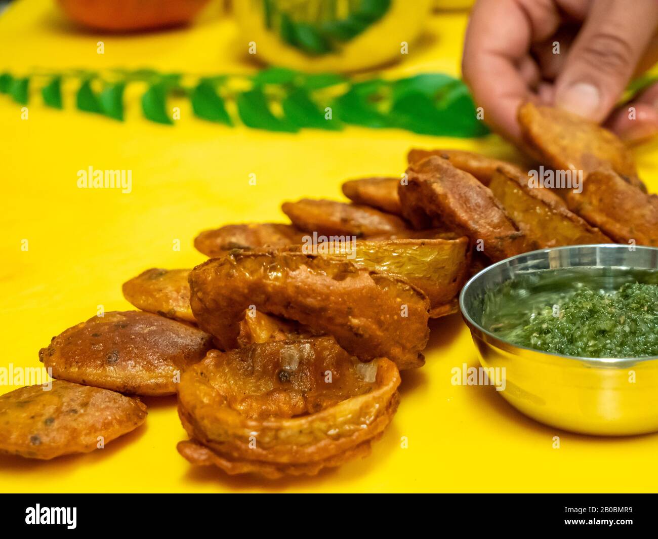 Primo piano con anelli di cipolla fritti indiani e kebab di agnello con chutney di menta e erba su un tagliere giallo brillante. Foto Stock