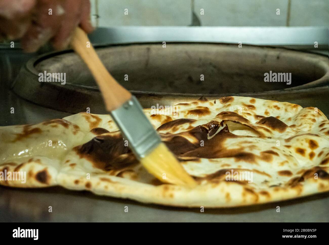 Un pane Naan cotto al forno di Tandoori viene spazzolato con burro fuso su una superficie di lavoro della cucina. Foto Stock