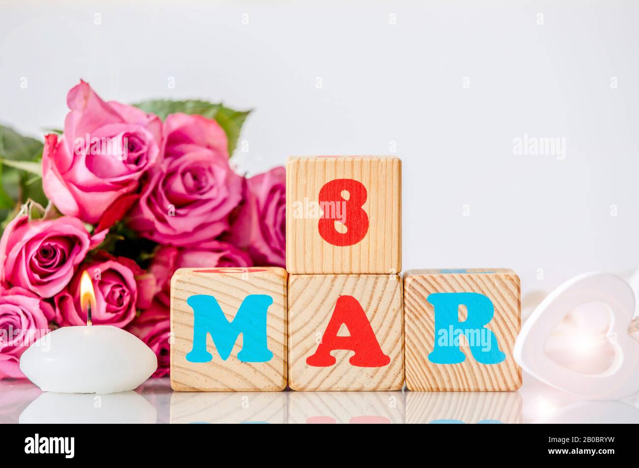 Calendario Internazionale della Giornata della Donna sfondo biglietto d'auguri. Con cuore di legno, rilassante candela a fuoco e bouquet decorativo rosa rosa sullo sfondo. Foto Stock