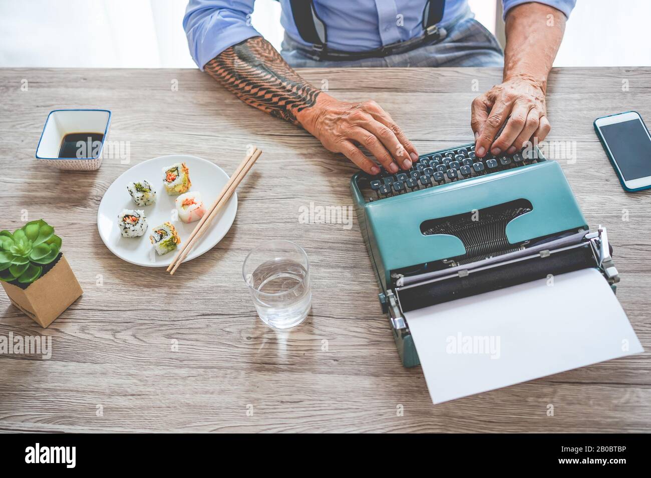 Uomo d'affari alla moda tatuato mangiare sushi a pranzo mentre si lavora - Senior imprenditore scrivere con macchina da scrivere vintage - tendenze alimentari e hippster w Foto Stock