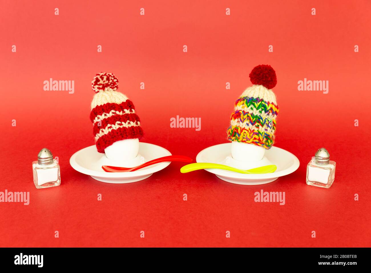 Divertente concetto di colazione con uova sode che portano cappelli di lana lavorato a maglia su sfondo rosso Foto Stock
