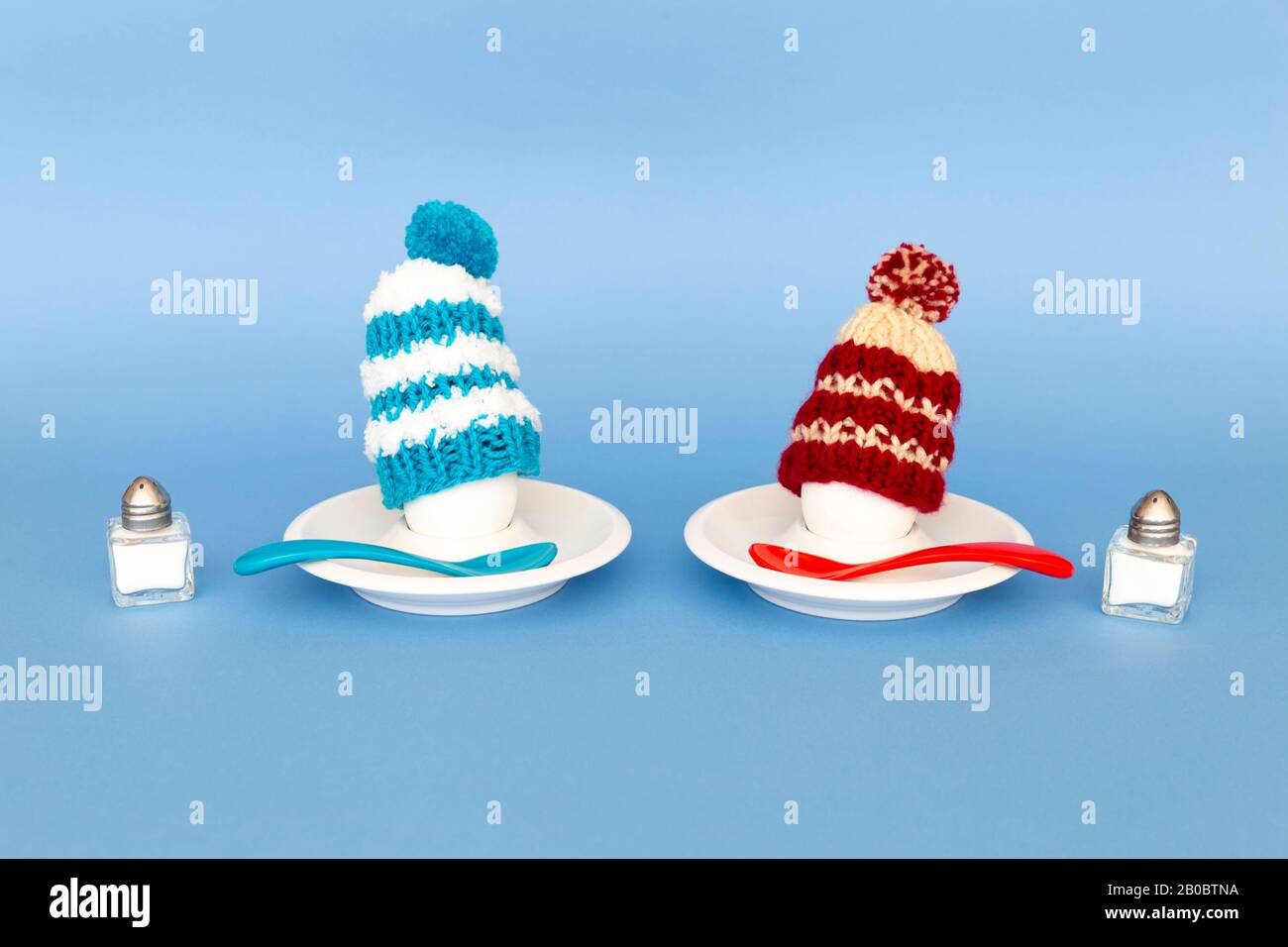 Divertente concetto di colazione con uova sode che portano cappelli di lana lavorato a maglia su sfondo blu Foto Stock