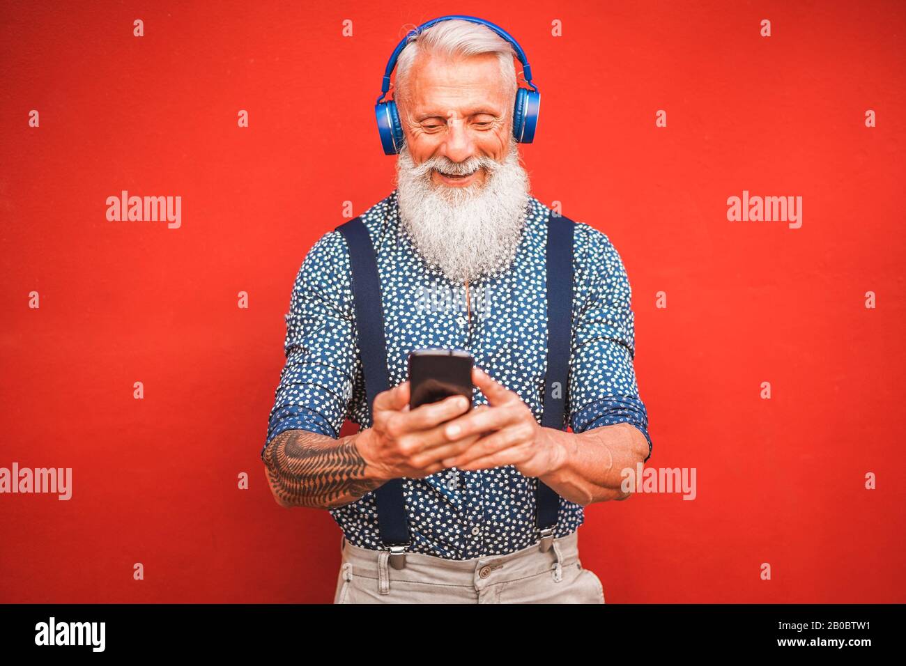Uomo di tendenza che utilizza l'app per smartphone con backgorund rosso - uomo di moda maturo divertirsi con le nuove tendenze tecnologia - Tech e gioiosi anziani lifes Foto Stock
