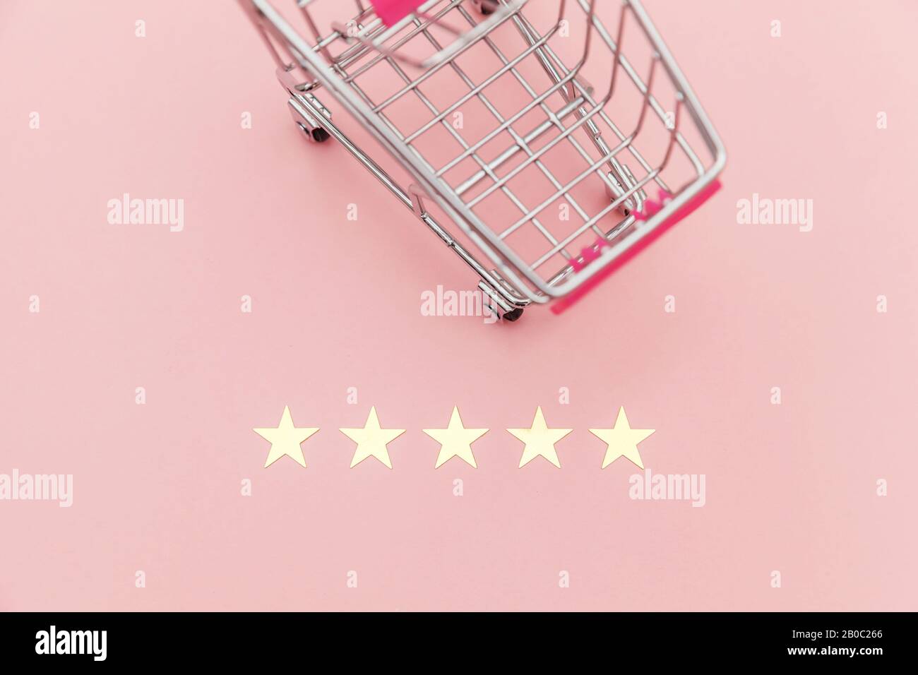 Piccolo supermercato negozio di alimentari carrello per lo shopping giocattolo con ruote e 5 stelle rating isolato su sfondo rosa pastello. Valutazione e revisione online degli acquisti al dettaglio da parte dei consumatori Foto Stock