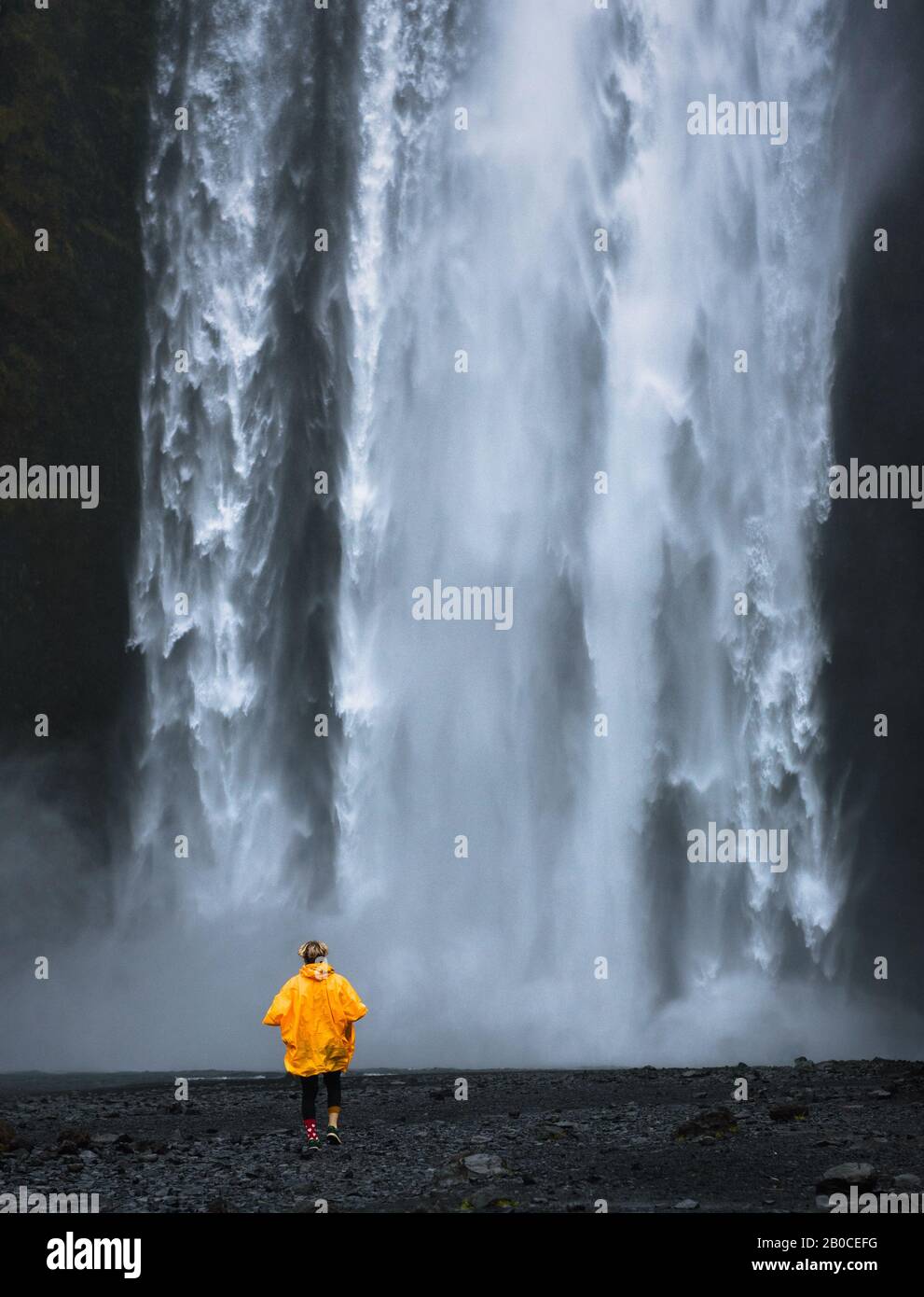 Turistico indossando un impermeabile giallo cammina verso la cascata Skogafoss in Islanda Foto Stock