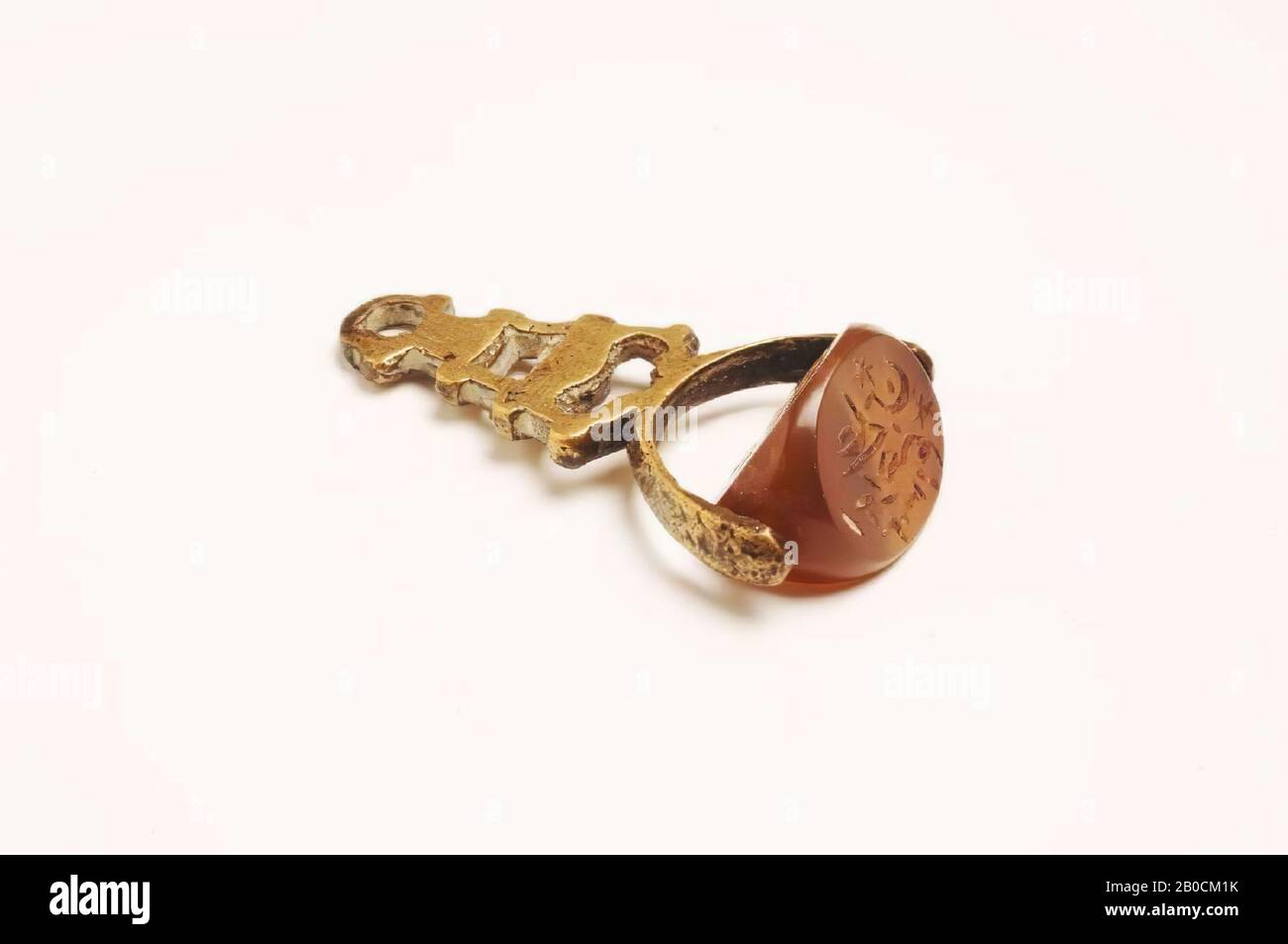 Un sigillo a tre lati di colore rosso-marrone trasparente calcedone. La guarnizione è forata longitudinalmente e fissata a un supporto di sospensione in bronzo. Il timbro è leggermente danneggiato su entrambi i lati. Su tutti e tre i lati è scritto arabo, completato con asterischi su due lati., Sigillo, iscrizione, pietra, calcedone, metallo, bronzo, L 4,2 cm, W 1,3 cm, H 2,2 cm, periodo islamico 600-1200 ad, Iraq Foto Stock