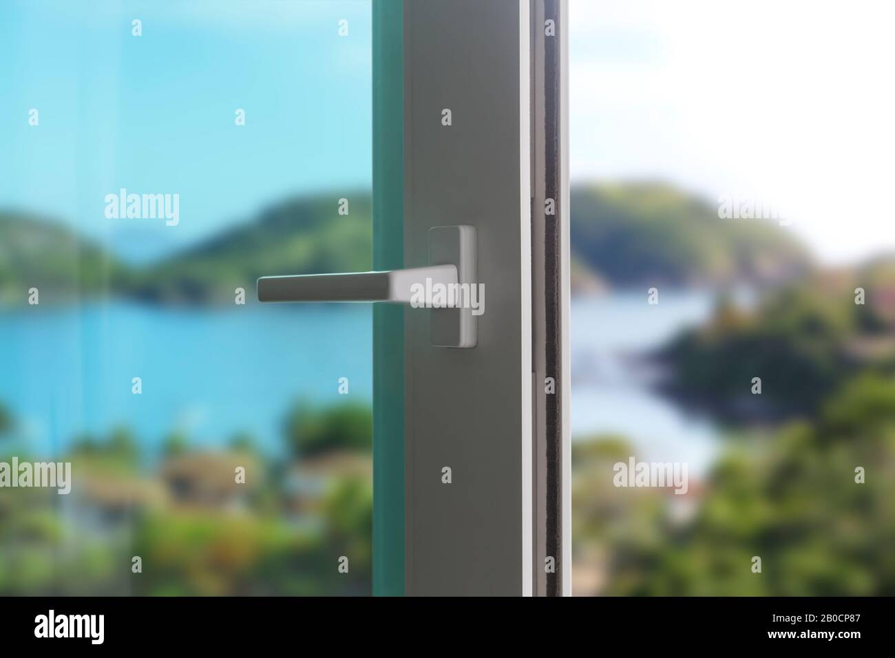 Porta scorrevole di un balcone. Primo piano della serratura sulla porta con un bel paesaggio di sfondo. Porta in PVC bianco e vetro di sicurezza. Foto Stock