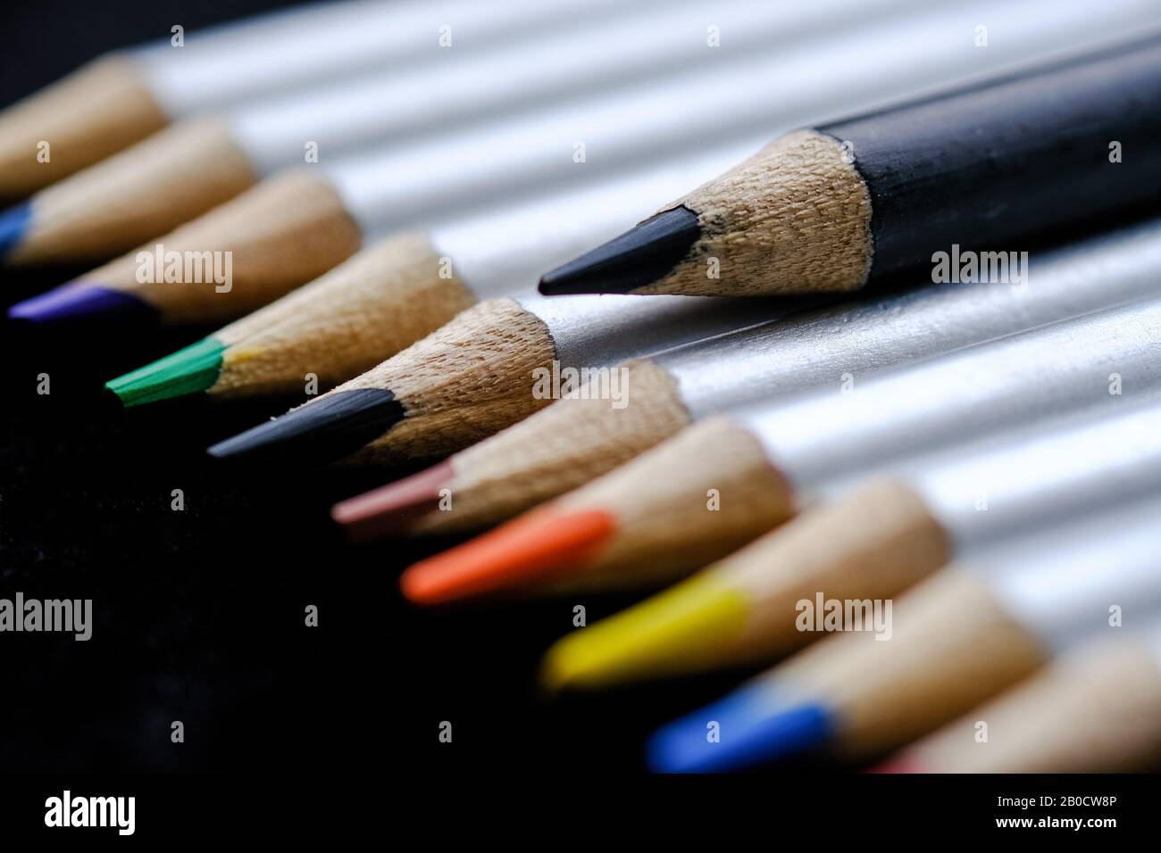 Set di matite colorate con una matita nera che si alza sopra e si alza dagli altri Foto Stock