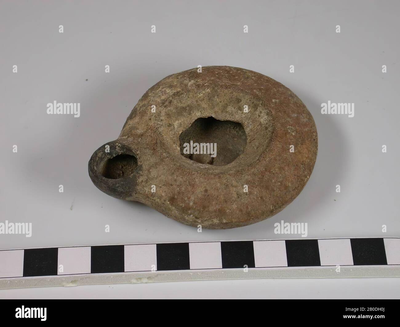 La lampada ha una base piatta. Le pareti hanno una forma leggermente convessa. Il bordo scorre quasi orizzontalmente verso l'interno e l'estremità è inclinata verso il basso. Il beccuccio è una sporgenza della forma circolare di base della lampada. Il colore è rosso con molte macchie bianche e scolorimento nero intorno al beccuccio a causa della bruciatura. Non c'è decorazione, stoviglie, ceramica, D max 6,3 cm, H 2 cm, D base 3,5 cm, D bordo 3,6 cm, D beccuccio 1,2 cm, periodo romano 63 a.C. - 324 d.C., Palestina Foto Stock