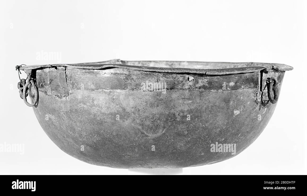 Ampia scatola in bronzo con pareti lisce e curve e fondo con ammaccature. Bordo inclinato stretto, eccellente. Al di sotto del bordo originario è stata originariamente prevista una fascia di ferro, le cui tracce sono ancora visibili. Anche sotto il cerchio 3 anelli, più tardi. Due si chiudono insieme, uno più piccolo e uno più grande. Il più piccolo con una coppiglia attaccata, quello più grande pure. Un terzo occhio piccolo, fissato allo stesso modo ad una terza distanza circonferenziale. Inoltre, altri 4 fori sotto il bordo per il nastro di fissaggio o ancora più occhielli. Danneggiato, parzialmente riparato con piastre saldate di bronzo in tempi antichi. Interno coperto di bianco Foto Stock