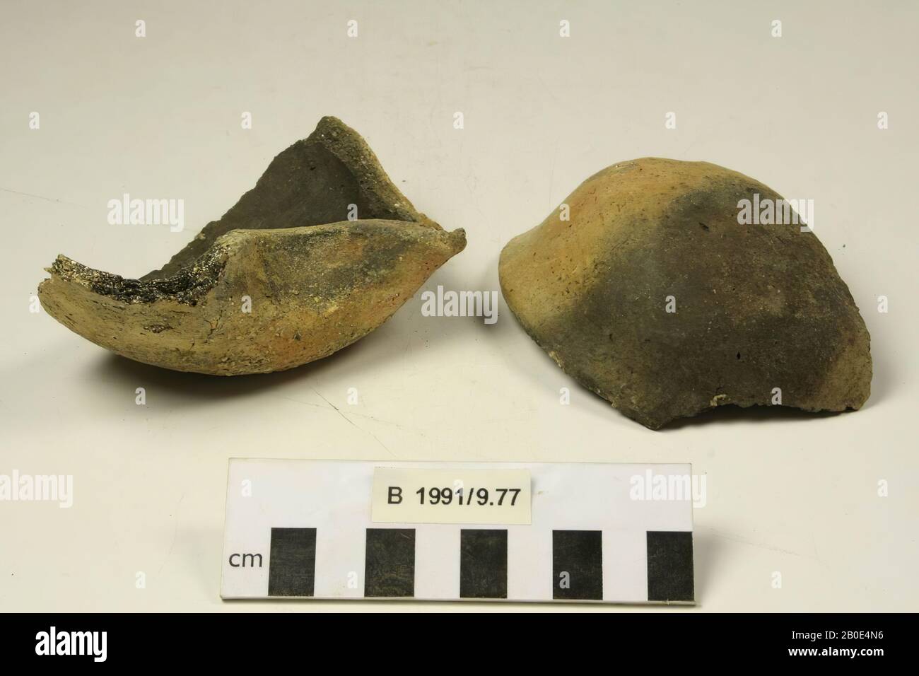 Una lampada di olio di terracotta, spezzata in 2 pezzi. Il fondo è convesso e passa attraverso una curva rotonda in una parete bassa che è inclinata verso l'esterno. Il bordo è piegato verso l'esterno e appiattito all'esterno. Su un lato il bordo e la parete sono pizzicati su un beccuccio. Realizzato a mano. L'argilla è di colore grigio e arancione, ha una consistenza media ed è agglutinata con calce, sabbia media e parti vegetali. All'esterno un rivestimento arancione con tracce di fuoco grigio scuro, fori o stampe di inclusioni, piccole crepe e sporco grigio-beige. Sotto i binari di sfregamento orizzontali del bordo. Sul fondo una superficie irregolare con Foto Stock