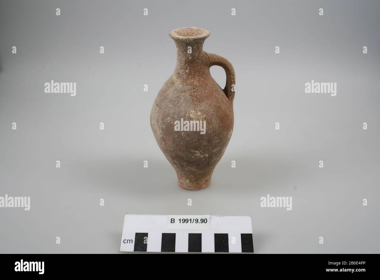 Una piccola bottiglia di terracotta con fondo piatto. La parete corre concava verso l'alto e si fonde in un corpo ovale allungato con un collo alto concavo. Una maniglia verticale è fissata alla spalla e al collo. Il bordo è verso l'esterno ed è immaturo. Fabbricato sulla ruota. Il fondo è tagliato con una corda. L'argilla è di colore rosso chiaro, ha una consistenza fine ed è agglutinata con calce e sabbia fine. All'esterno un rivestimento arancione, parzialmente scuro scolorito e coperto con un tocco bianco-giallo. Sulla parte inferiore della diagonale della parete raschiando o lucidando le tracce. Sulla parte inferiore dell'impugnatura è presente un viola Foto Stock
