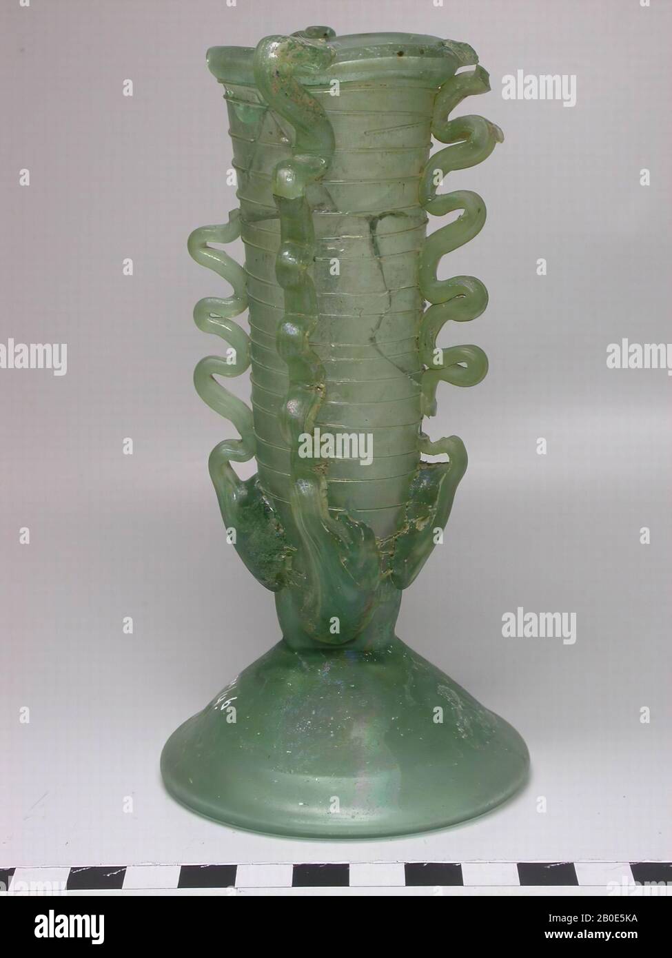 Tazza oblunga in vetro verde su un piede conico grande. La tazza è avvolta a spirale con filo di vetro fine. Inoltre, quattro fili di vetro spesso corrono verticalmente sopra la tazza dall'alto verso il basso, terminando in pezzi spessi a forma di foglia., beffa, vetro, H 14.5 cm, Libano Foto Stock