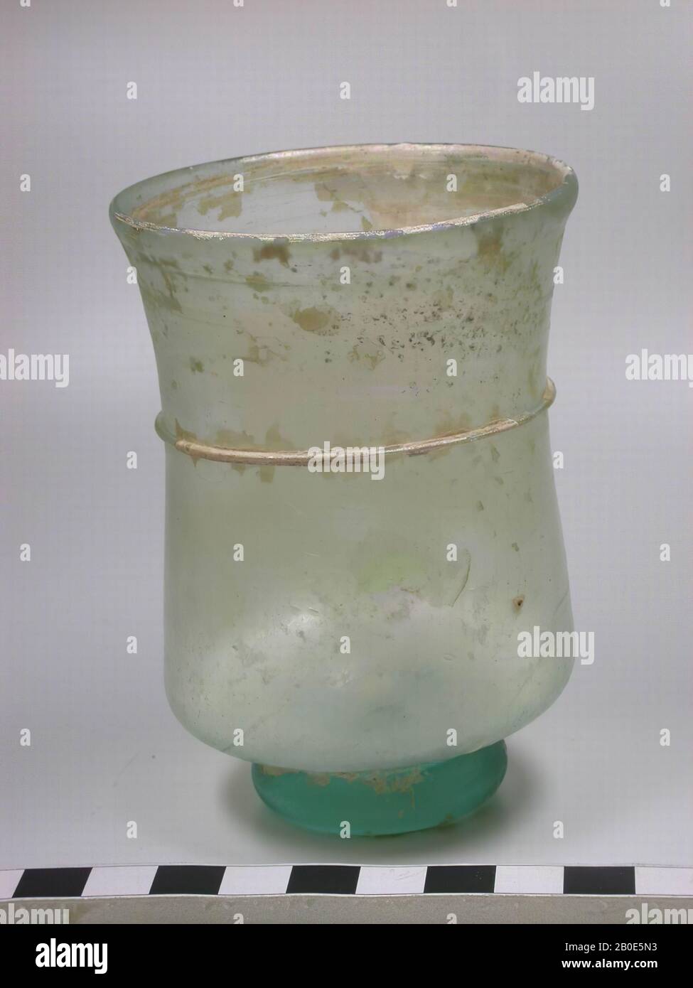 Bicchiere di vetro verde chiaro tardo romano. Con un bordo della bocca curvo verso l'esterno, corpo cilindrico con un profilo leggermente concavo. Anello di supporto robusto e pesante che è stretto. Intorno alla metà superiore un filo di vetro sottile è avvolto quasi orizzontalmente intorno alla tazza., beffa, vetro, H 10 cm, Periodo tardo romano 135-324 ad, Siria Foto Stock