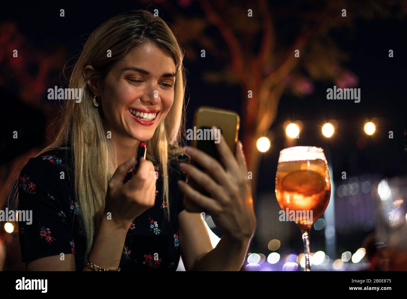 Giovane donna che applica il rossetto al caffè all'aperto Foto Stock