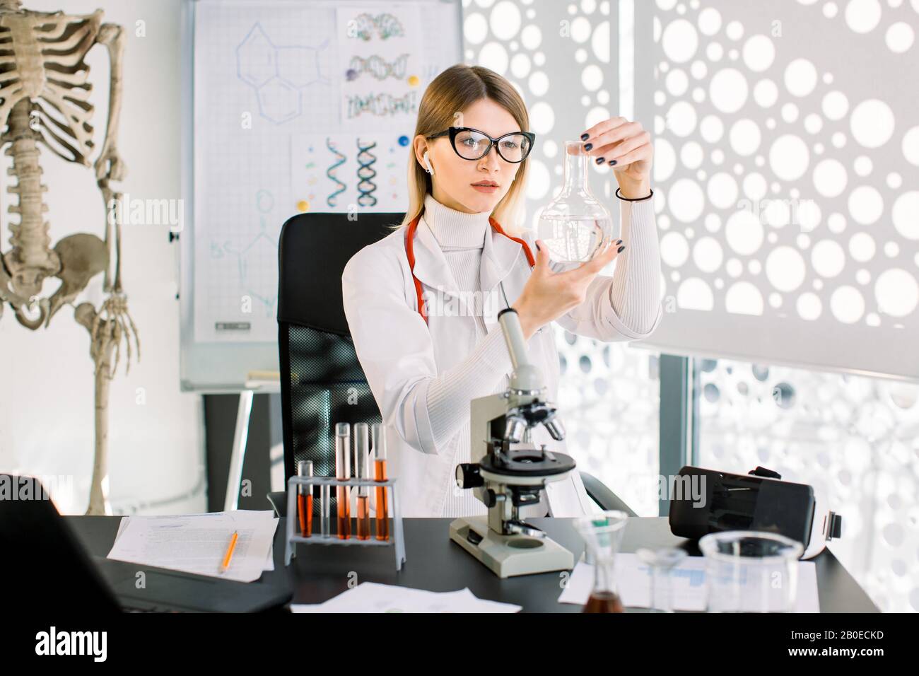 Ricercatore medico farmacista scienziato femminile che conduce un esperimento in un laboratorio, esaminando una nuova sostanza, medicina, guardando il pallone in Foto Stock