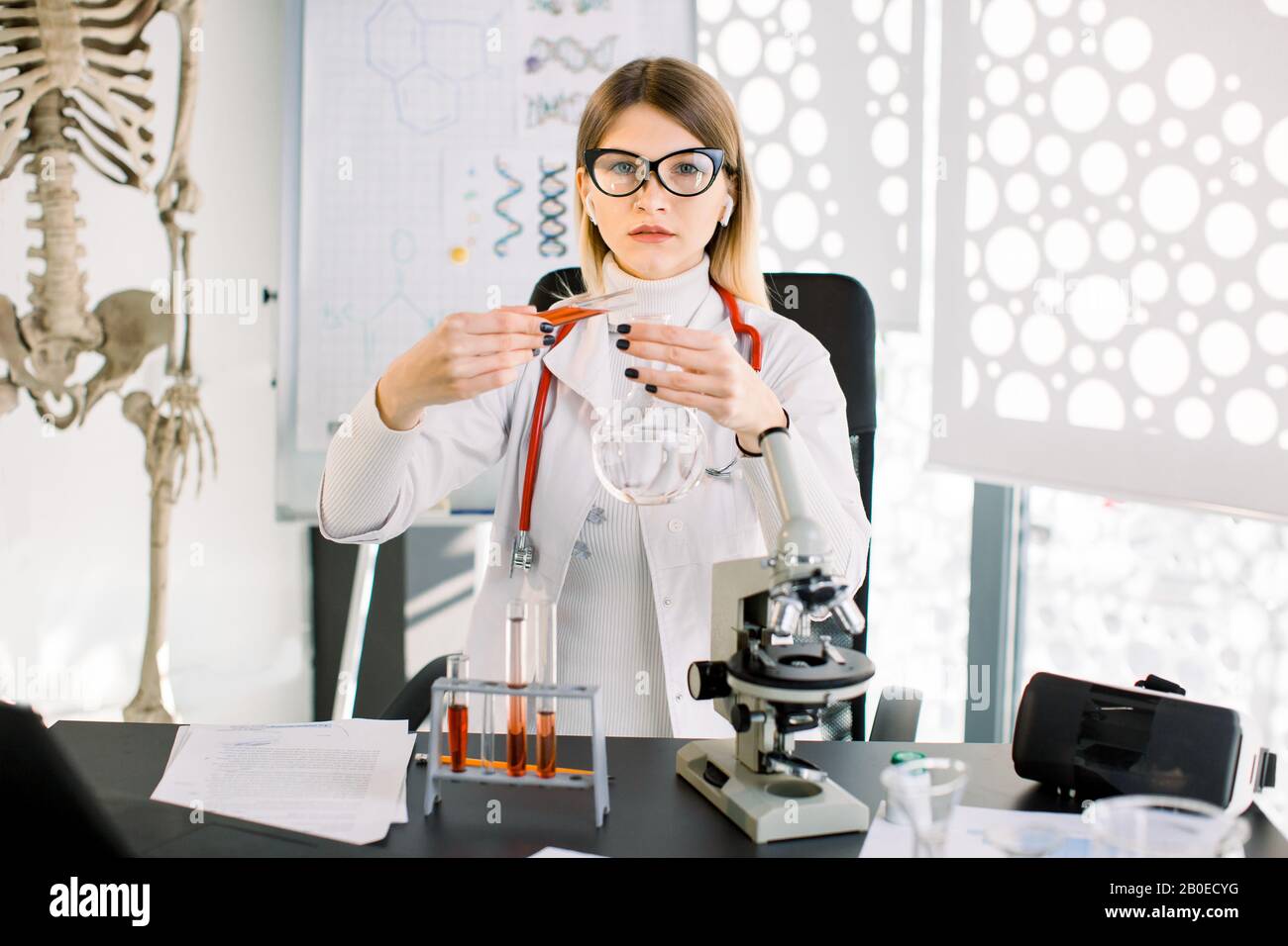 Abbastanza caucasica donna ricercatore medico chimico con vetro attrezzatura nel laboratorio. Donna scienziato professionale purificante soluzione rossa forma tubo in Foto Stock