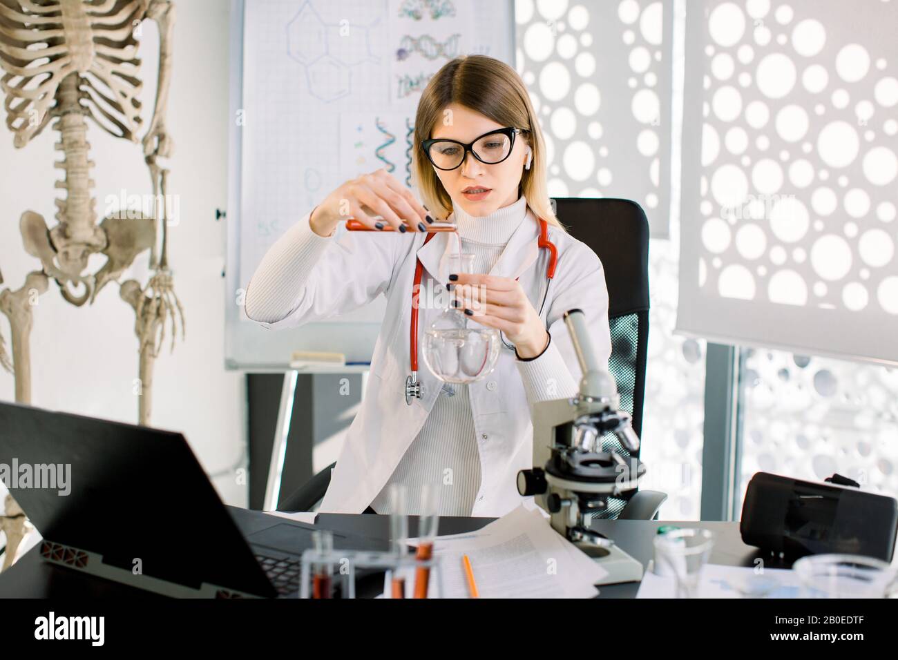 Giovane attraente scienziato concentrato donna in occhiali protettivi e camice bianco ricerca nel laboratorio chimico scientifico medico Foto Stock