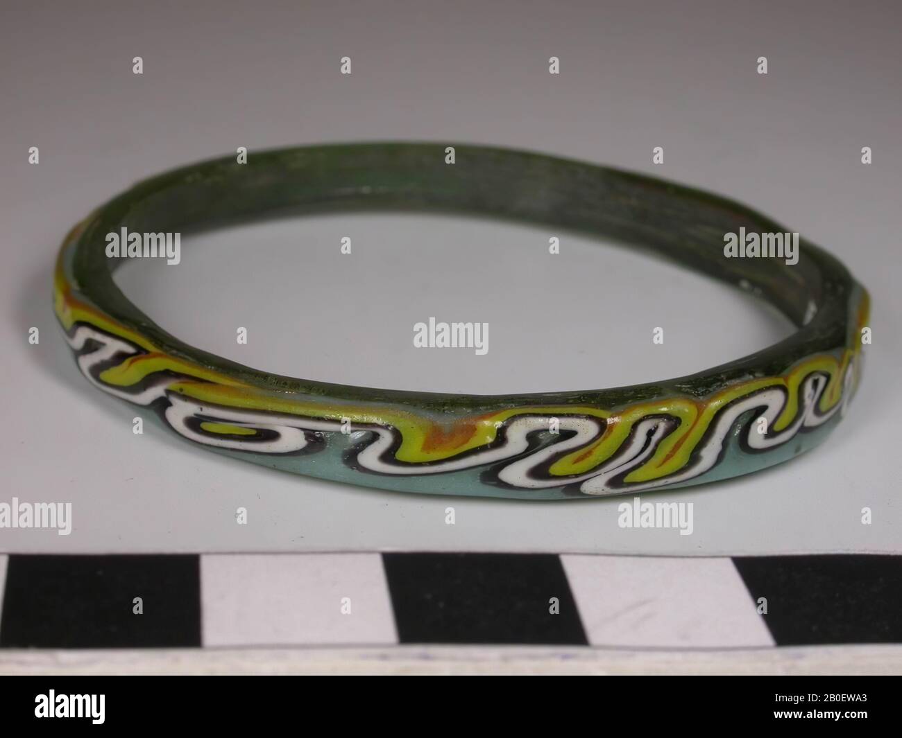 Bracciale, un bracciale rotondo irregolare in vetro verde oliva trasparente. Decorato con un filo di vetro fuso meandering di vetro opaco nei colori turchese, nero, bianco, giallo e arancione., bracciale, vetro, filo di vetro manipolato, diam. 6,3 cm, Periodo copto, 3rd Secolo islamico, Egitto Foto Stock