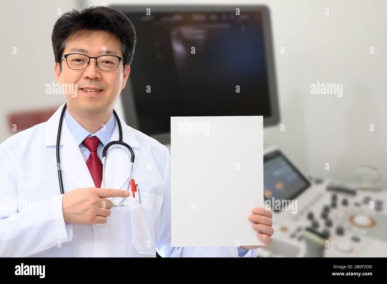 Un medico di sesso maschile che tiene una bacheca di fronte a un dispositivo diagnostico a ultrasuoni Foto Stock