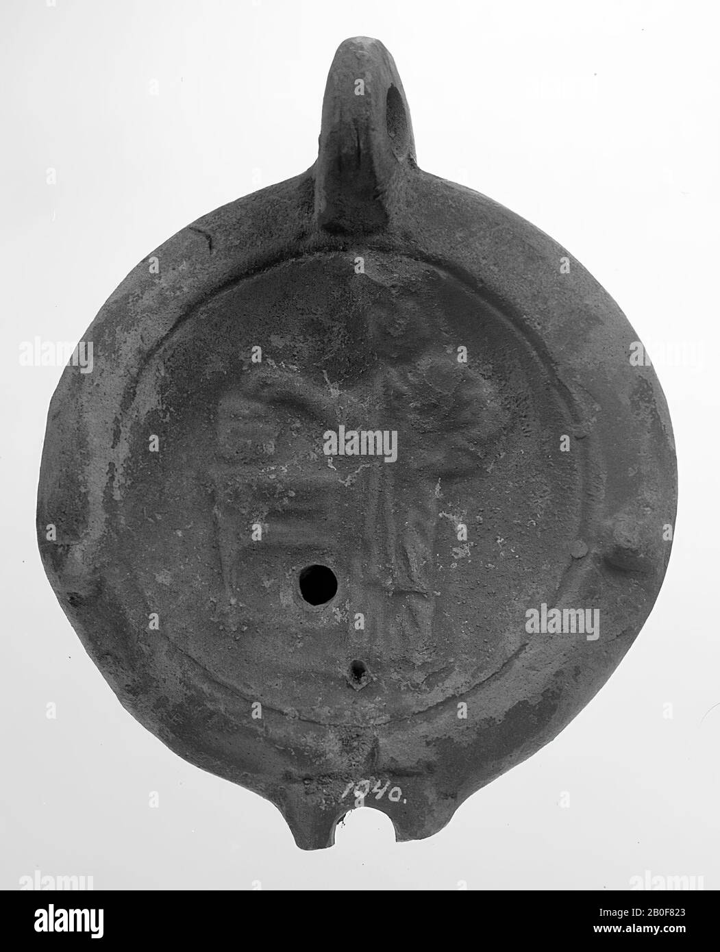 Lampada annidata rossa con corpo rotondo e piedistallo. Lo specchio rotondo concavo è circondato da un cerchio incassato e decorato con Athena che si trova davanti a un tavolo con oggetti. Il piccolo foro di riempimento si trova sotto il centro. Su entrambi i lati della spalla è presente un lavaggio verticale. Il beccuccio piccolo e smussato era arrotondato e aveva un piccolo foro di fuoco. L'insorgenza è orizzontale. L'orecchio verticalmente attaccato è decorato con tacche, lampada ad olio, terracotta, terracotta, 4,7 x 10,7 x 8,7 cm, 2nd e 3rd secolo DC. 100-300 DC, Tunisia Foto Stock