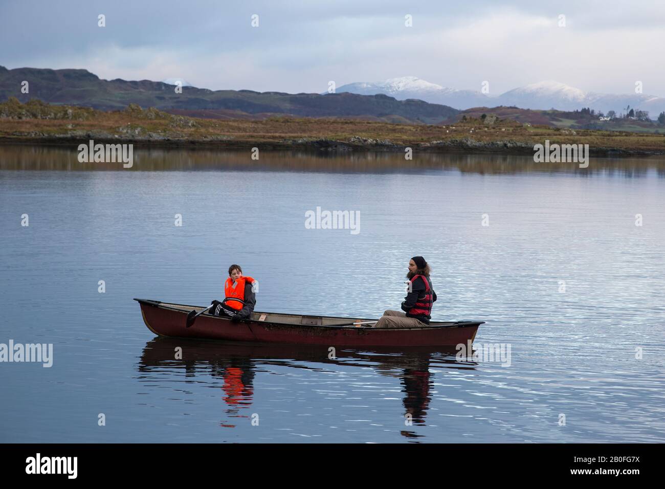 Padre e figlio canottaggio sulle acque fisse della baia di Ardmaddy il giorno di Natale in Scozia occidentale con le montagne innevate sullo sfondo Foto Stock