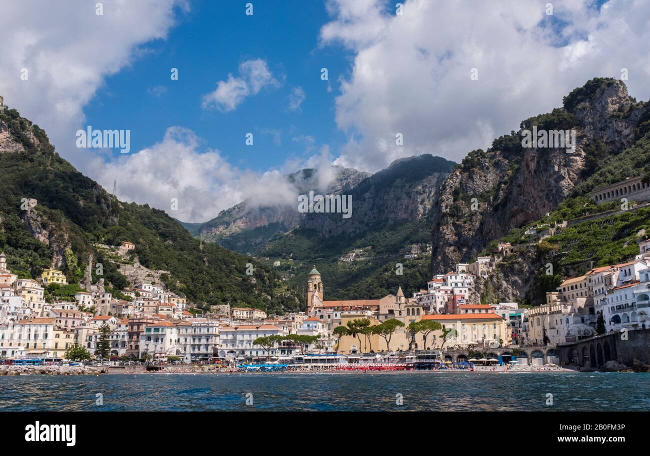 Il colorato villaggio di Amalfi visto dal mare, con montagne suggestive e cieli estivi sullo sfondo, sulla costa d'Italia Foto Stock