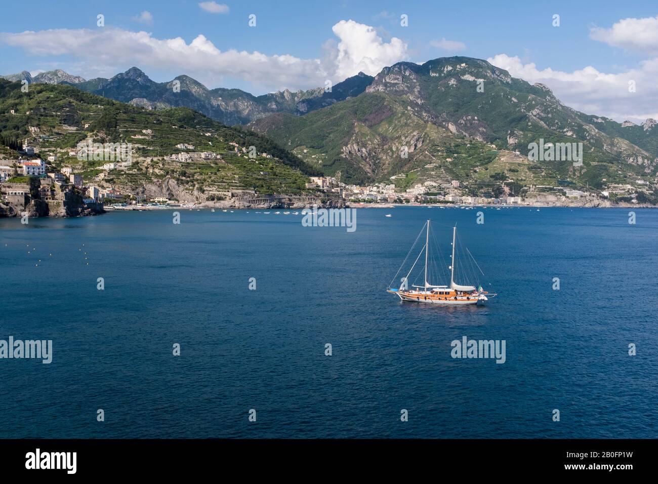 Uno yacht ancorato al largo della costiera amalfitana in una luminosa giornata estiva in Italia, con il paesaggio montano al di là. Foto Stock