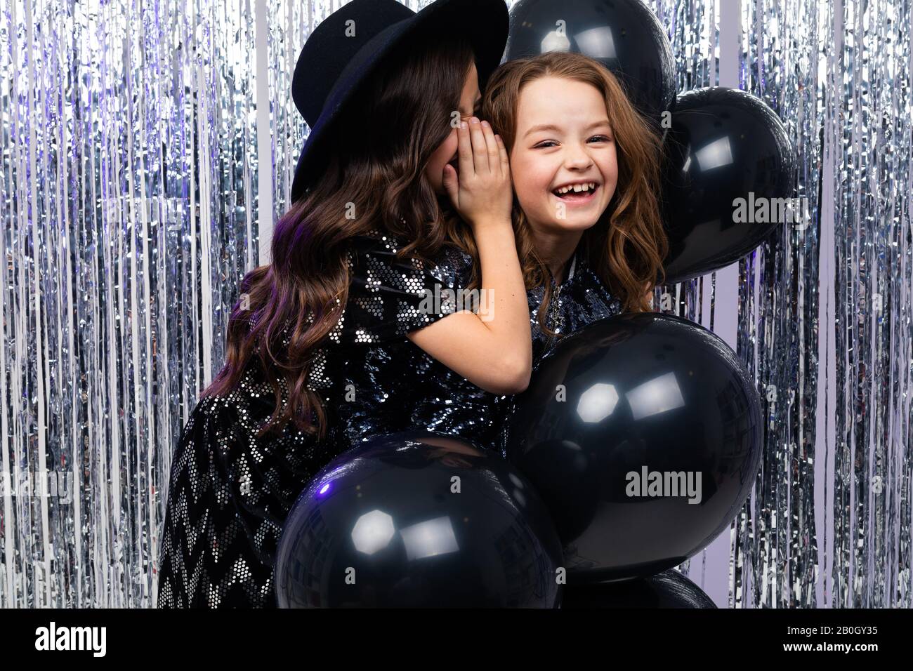 festa di compleanno. ragazze secrete in abiti festosi su uno sfondo lucido Foto Stock